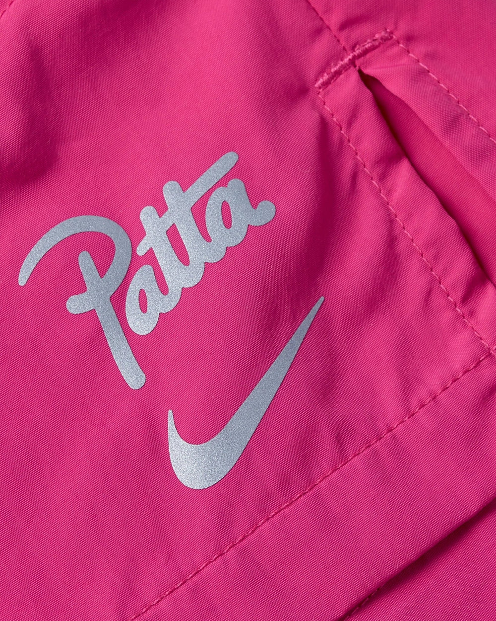 Detail of pink Nike x Patta Running Team shorts showing reflective Patta logo, Nike Swoosh, and pocket seam.
